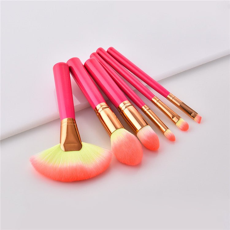 Makeup brush set with coral-pink handles and gold ferrules, including fan and round brushes