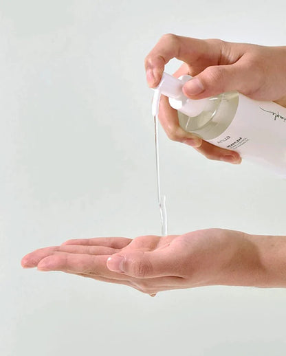 Cleansing oil dispenser pouring pale yellow oil onto hands for face cleansing
