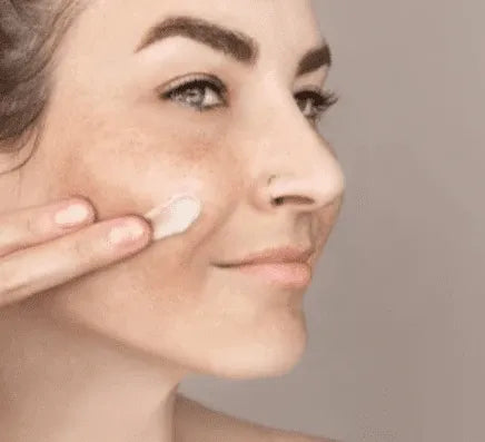 Skincare cream dabbed on cheek under an eye with fingers for dark spot removal
