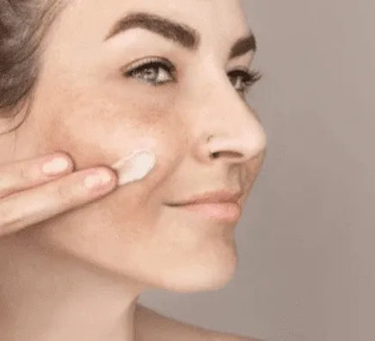Skincare cream dabbed on cheek under an eye with fingers for dark spot removal