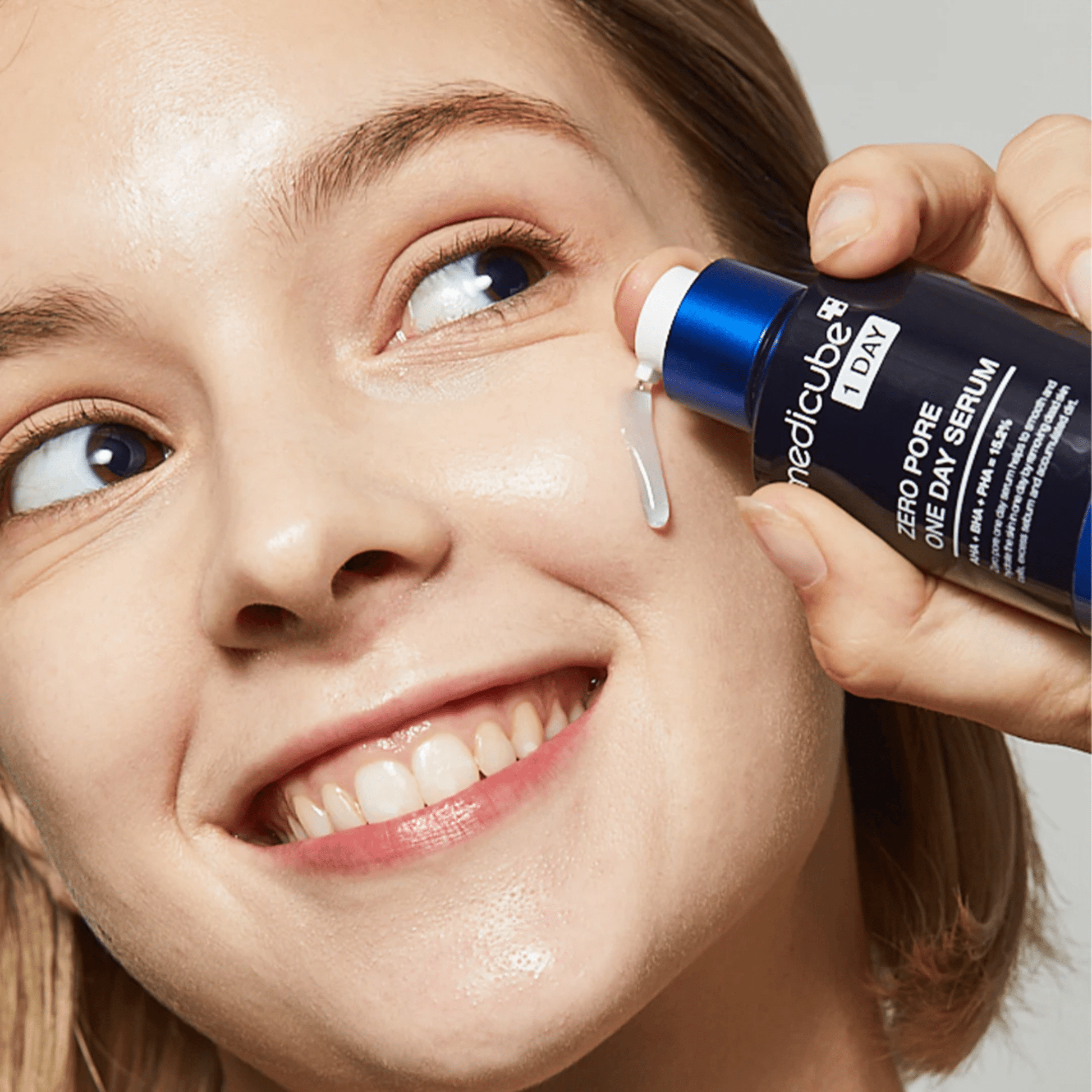Medicube pore-reducing serum bottle with dropper, held beside a woman's eye
