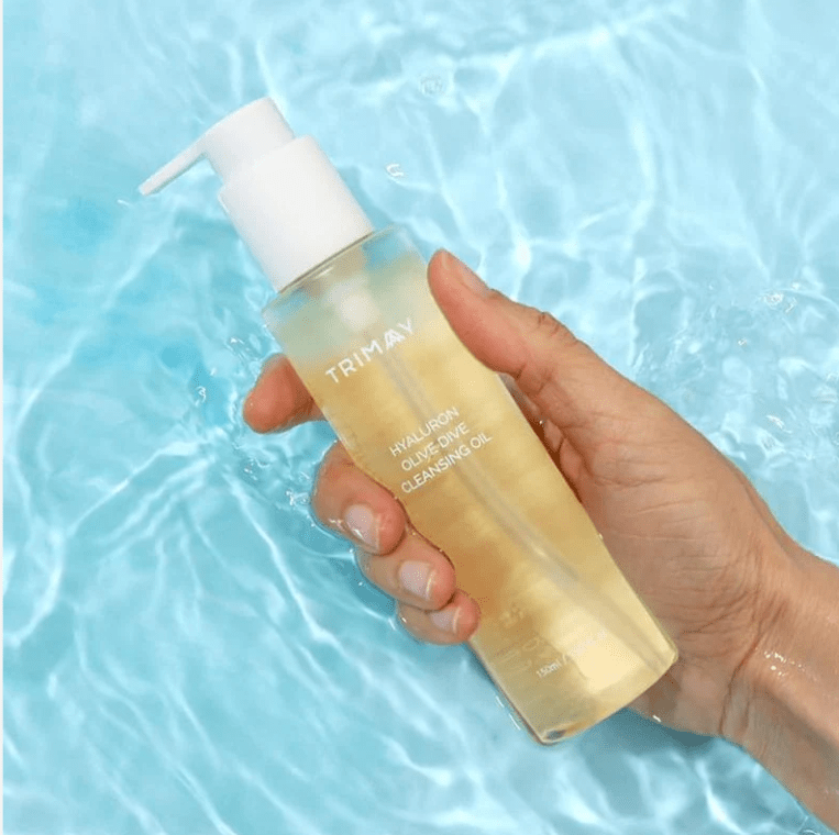 Gold-toned cleansing oil bottle with pump held over water